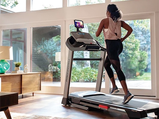 Woman running on treadmill in living room with floor-to-ceiling windows