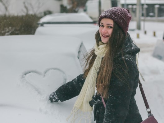 Young Woman Drawing a Heart on a Snow-Covered Car Windshield