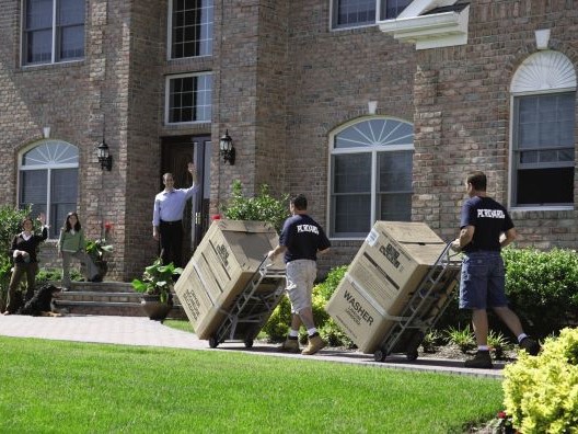 P.C. Richard Delivery Crew Wheeling Two Giant Boxes Into a Large House