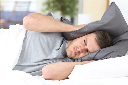 Man covering his ears with a pillow