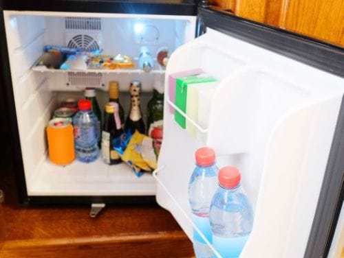 Open mini fridge filled with various drinks and snacks