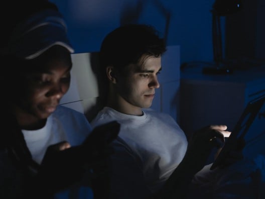 Couple in dark bedroom with their faces illuminated by screens