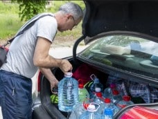 Man loading large plastic jugs of water into a car trunk
