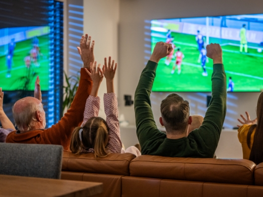 A family on a couch excitedly watching a soccer game on a TV.