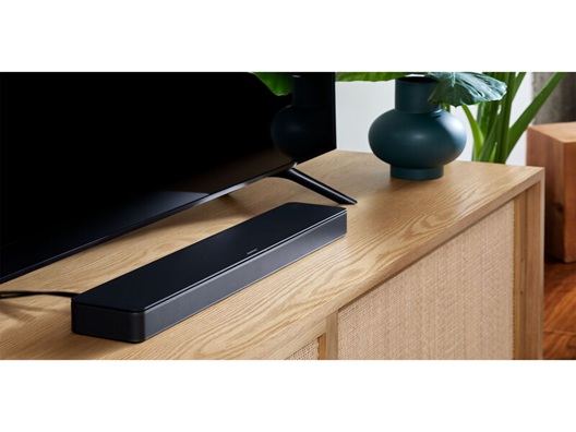 A soundbar with a wire coming out of the back of it on a TV stand, positioned below a TV.