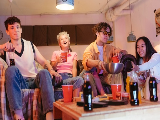 A group of people happily sitting on a couch with food drinks in front of them.