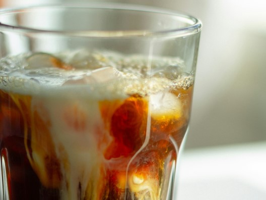 Closeup of a glass of brown soda with swirls of cream.