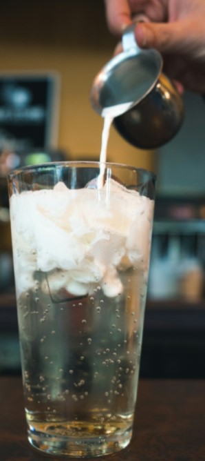 A glass of golden-colored soda with some cream being poured into it