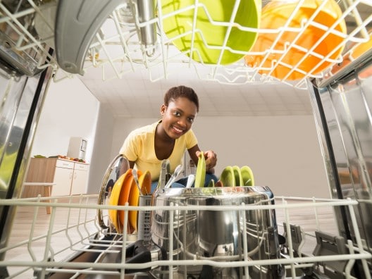 Black woman loading bright green and yellow dishes into a dishwasher