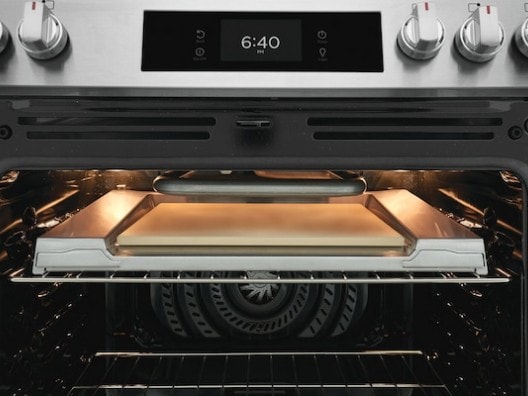 Open oven displaying pizza stone on top rack