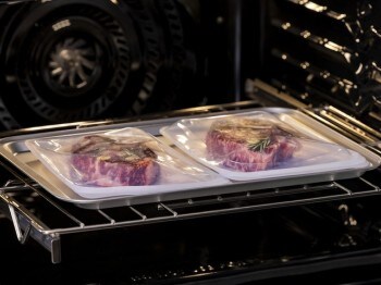 Interior of oven with two steaks vacuum-sealed in bags sitting on a baking sheet