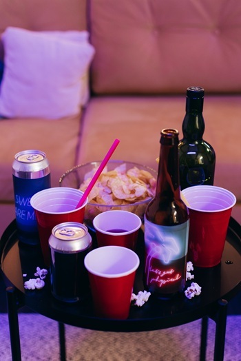 Cans, bottles, red cups, and chips in a bowl on a table.