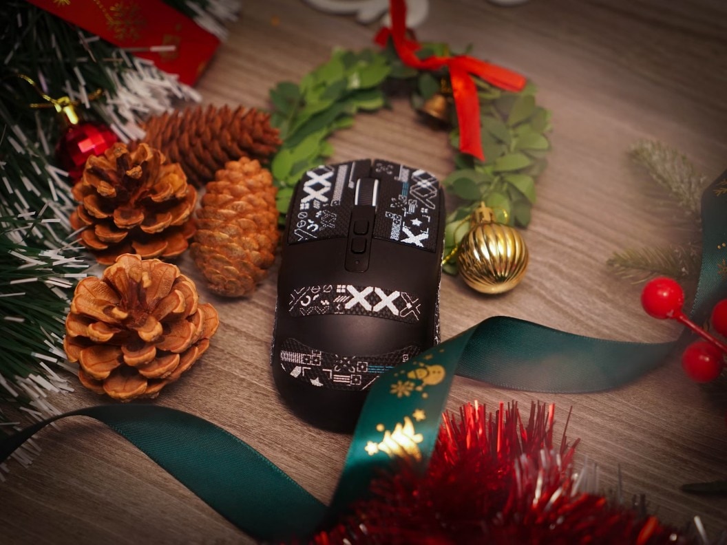 A mouse sitting on a wooden surface surrounded by holiday decorations.