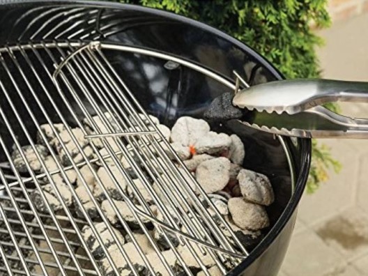 Tongs adjusting the charcoal in a charcoal grill.