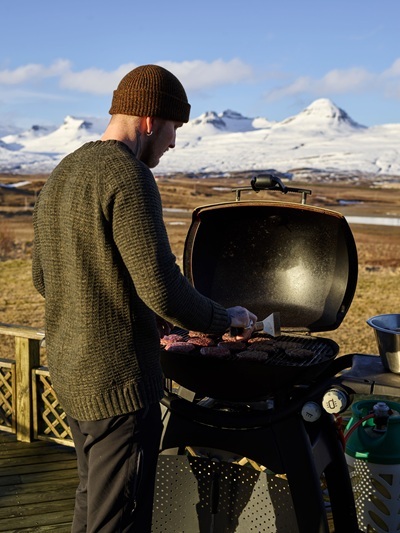 A man grilling on a gas grill in front of a snowy landscape.