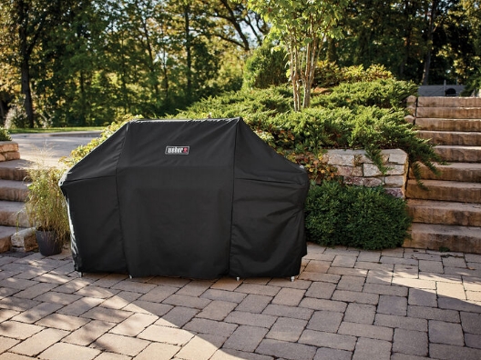 A grill, sitting outdoors, covered by a grill cover.