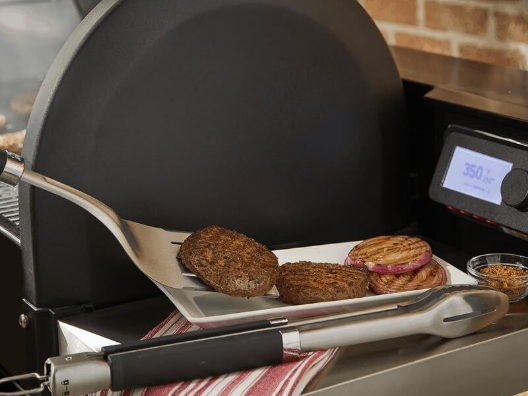 A spatula placing a cooked burger next to another on a plate on the side of a grill.