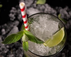 Crushed ice in a highball glass with a striped straw, mint, and lime slice