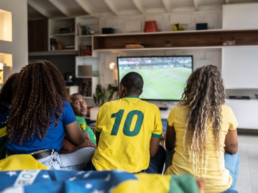 A group of people on a couch watching soccer on a TV.