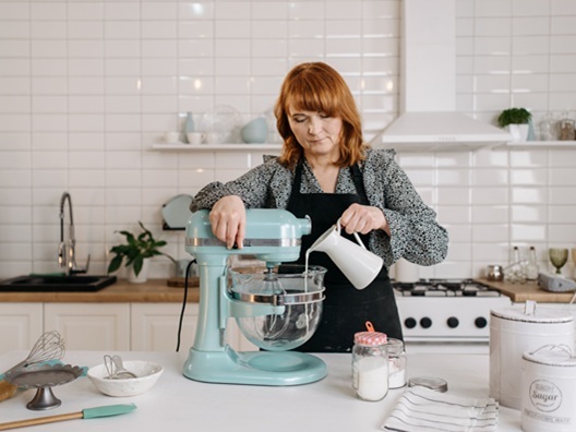 A woman pouring an ingredient into a stand mixer.