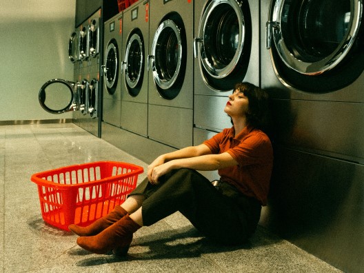 A melancholy woman sitting next to an empty laundry basket at a laundromat