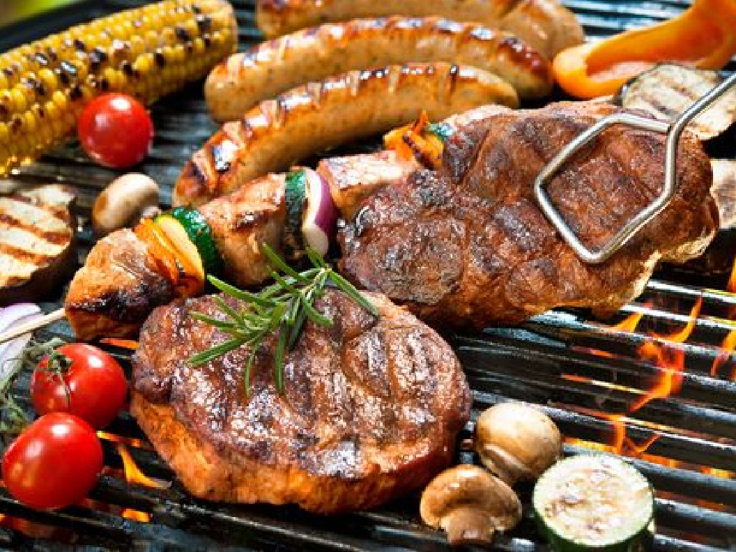 A close-up image of meats and vegetables on a grill being picked up by tongs.