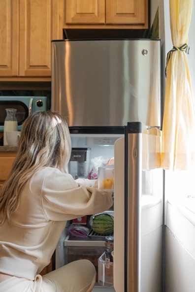 A woman kneeling in front of an open refrigerator and adjusting the items within.