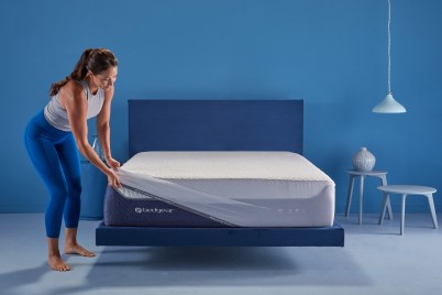 A woman stretching a mattress protector over a mattress