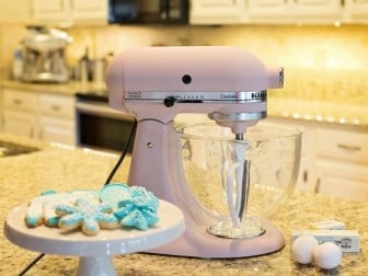 Pastel pink KitchenAid Stand Mixer in a kitchen with holiday cookies in foreground