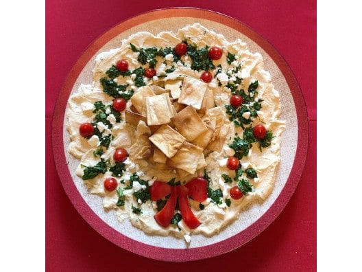 Platter of hummus, pita chips, tomatoes, and spinach in the shape of a wreath