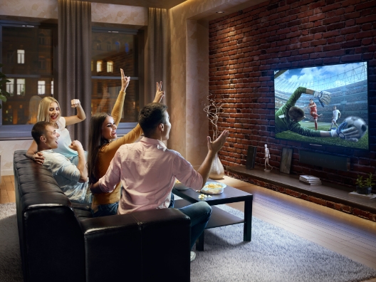 A group of people on a couch watching soccer on a TV.