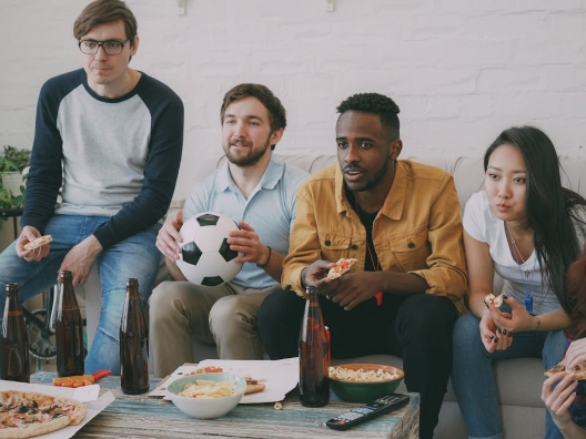 A group of people watching sports on a TV while drinking and eating.