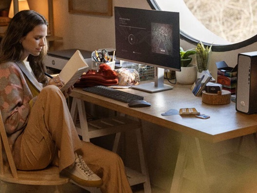 A woman sitting at a desk in front of a computer monitor and taking notes in a notebook.