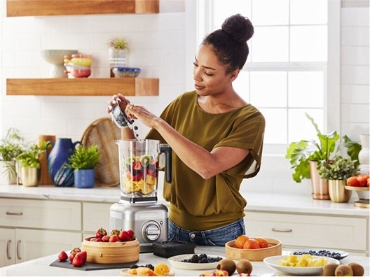 A woman loading up a blender with fruits.