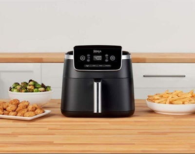 An air fryer on a table, surrounded by different foods.